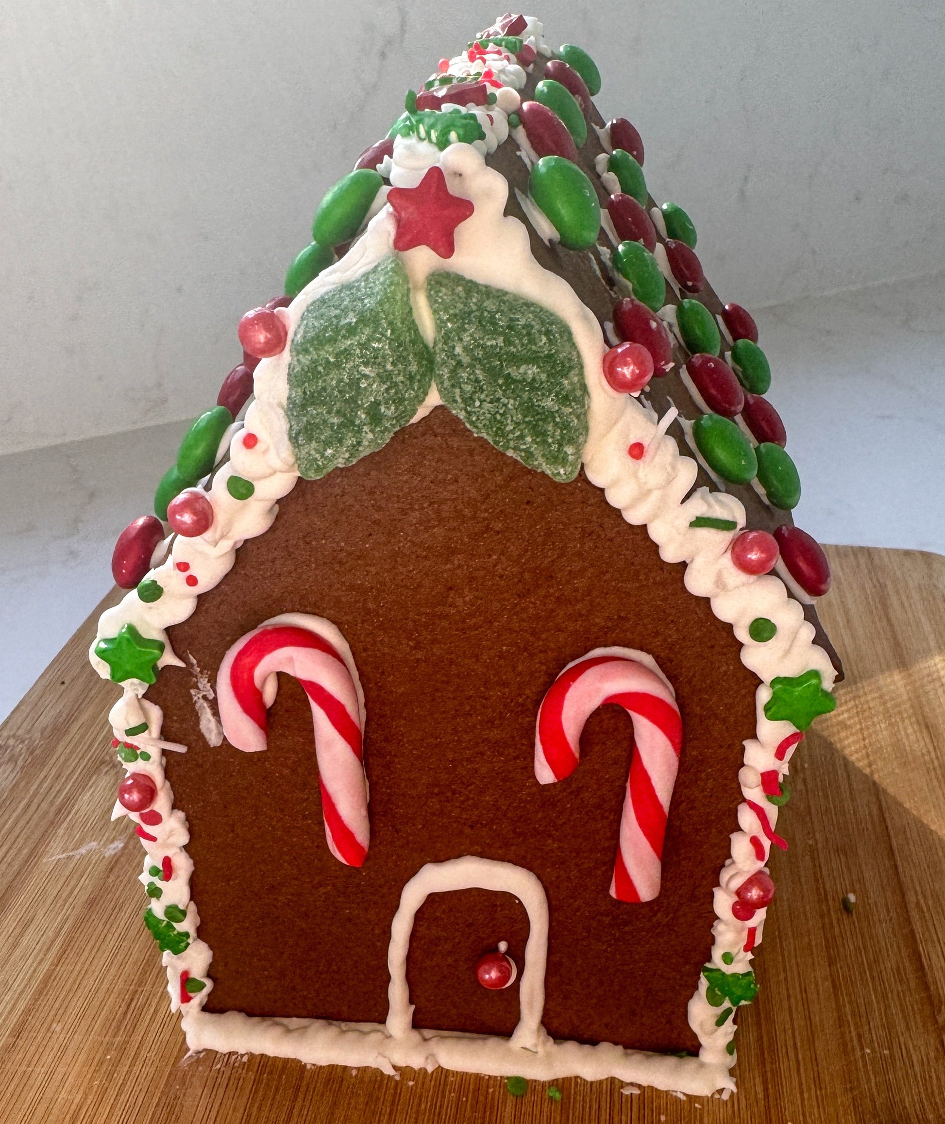 Gingerbread house with candy cane details on a wooden surface